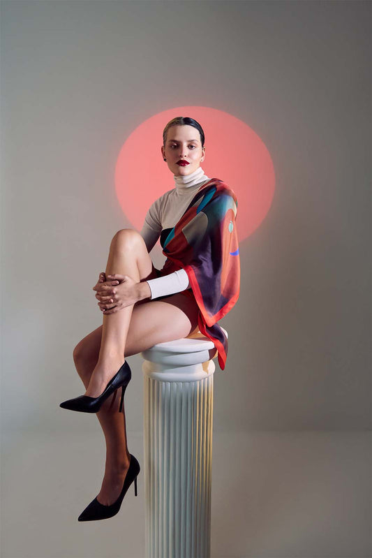 Model seated elegantly, wearing the Furor scented scarf from Freeque’s Hygieia Collection, set against a bold red circular backdrop