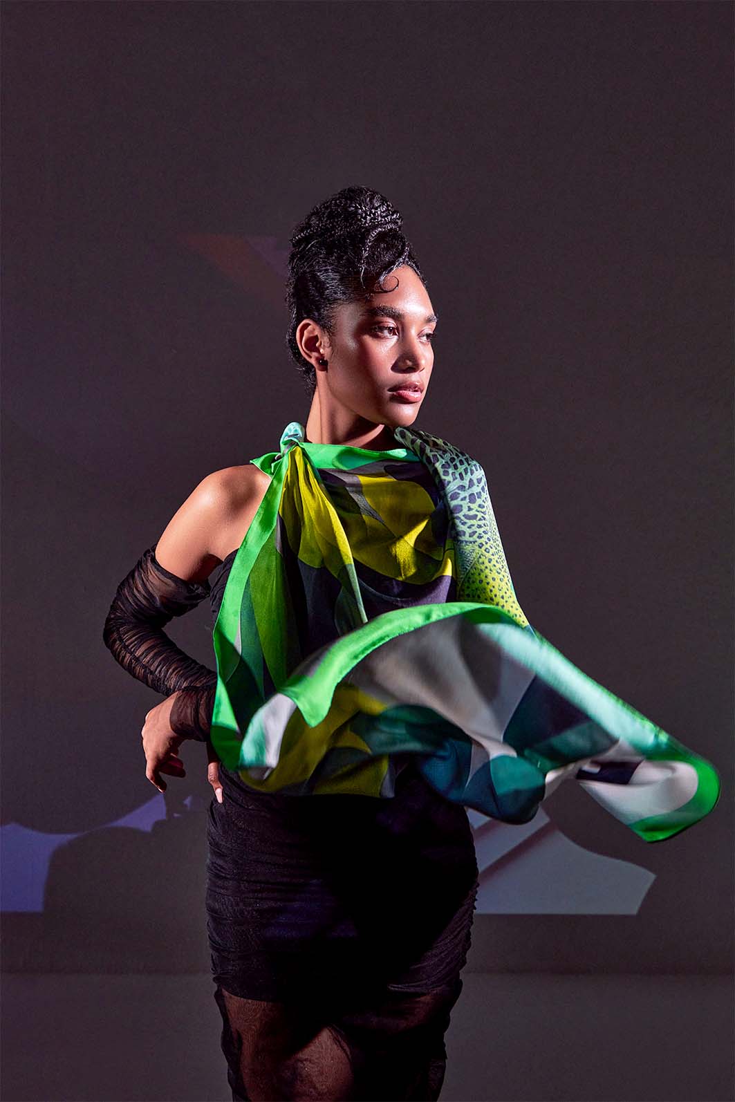 Model showcasing movement in Metamorphosis Transformation scarf with vibrant green and gray tones