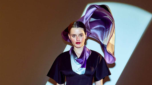 Model wearing Thánatos scented silk scarf in purple hues under dramatic lighting.