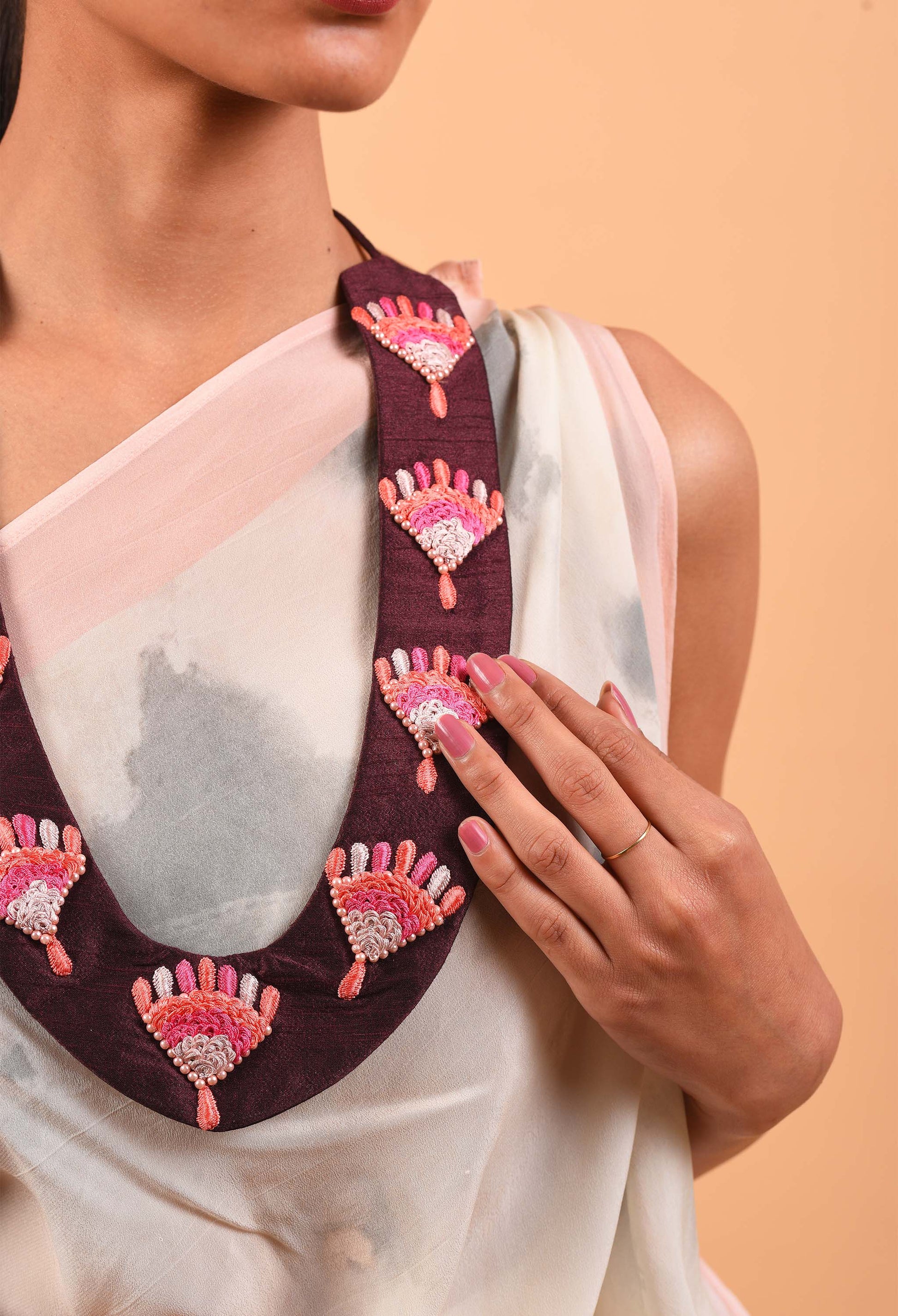 Close-up of Reign handcrafted necklace showcasing detailed beaded embellishments on maroon fabric
